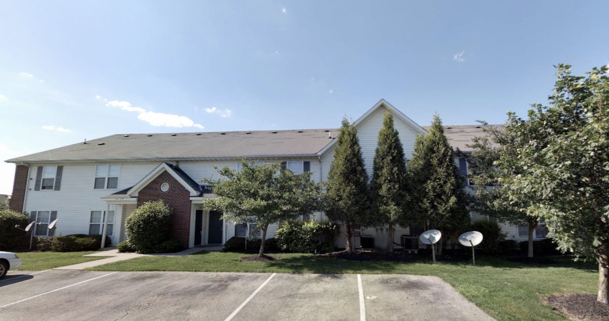 White-sided apartment building with brick entry and mature trees